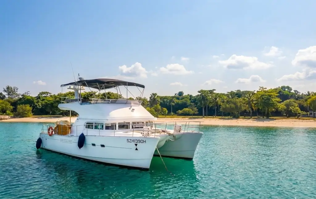 Lagoon 440 Power Catamaran - Island Yacht One Charter Singapore - A large white catamaran is anchored in clear turquoise water, with a sandy tropical beach and lush green trees in the background under a blue sky at ON...