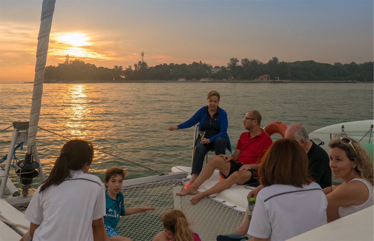 A group of people sitting on the deck of a yacht as the sun sets